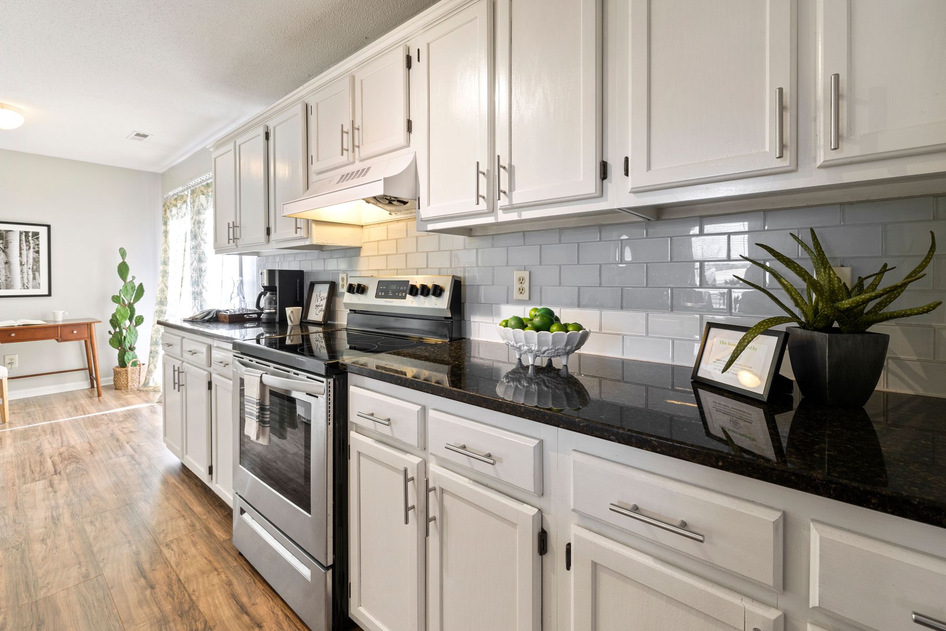 Bright modern kitchen with white cabinets, black countertops, and wood floors featuring stylish appliances.